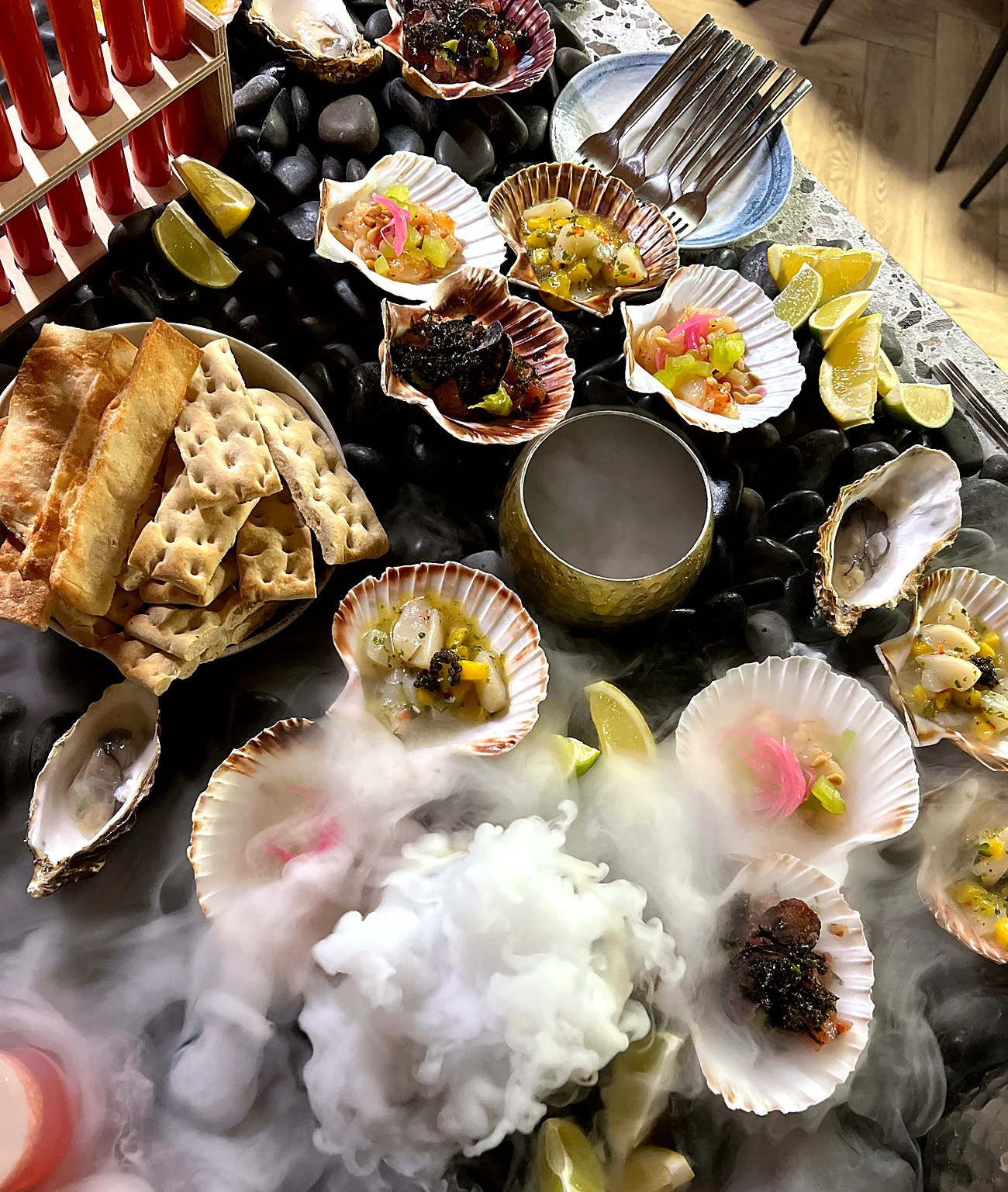 Scallops, oysters and lime on black stones under a cloud of nitrogen fog, seen from above